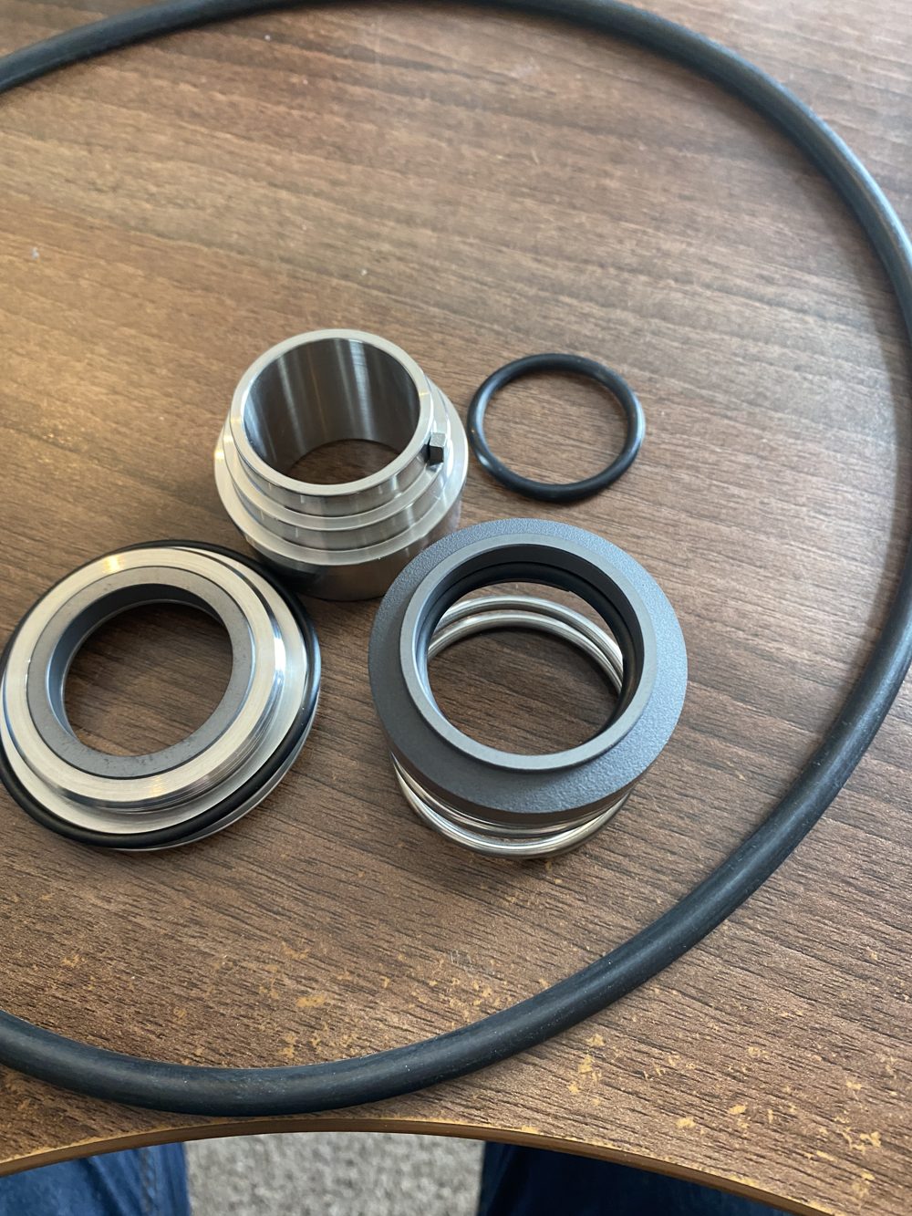 Mechanical seal components laid out on a wooden table: seal faces, a sleeve, a spring and O-rings