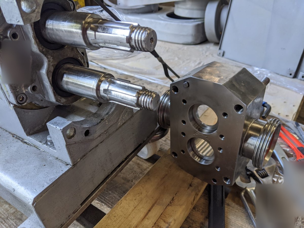 Two exposed rotary lobe pump shafts beside the separated housing with two circular openings on a workbench